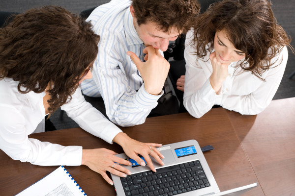 Young businesspeople sitting by table at office working together on laptop computer. High-angle view.